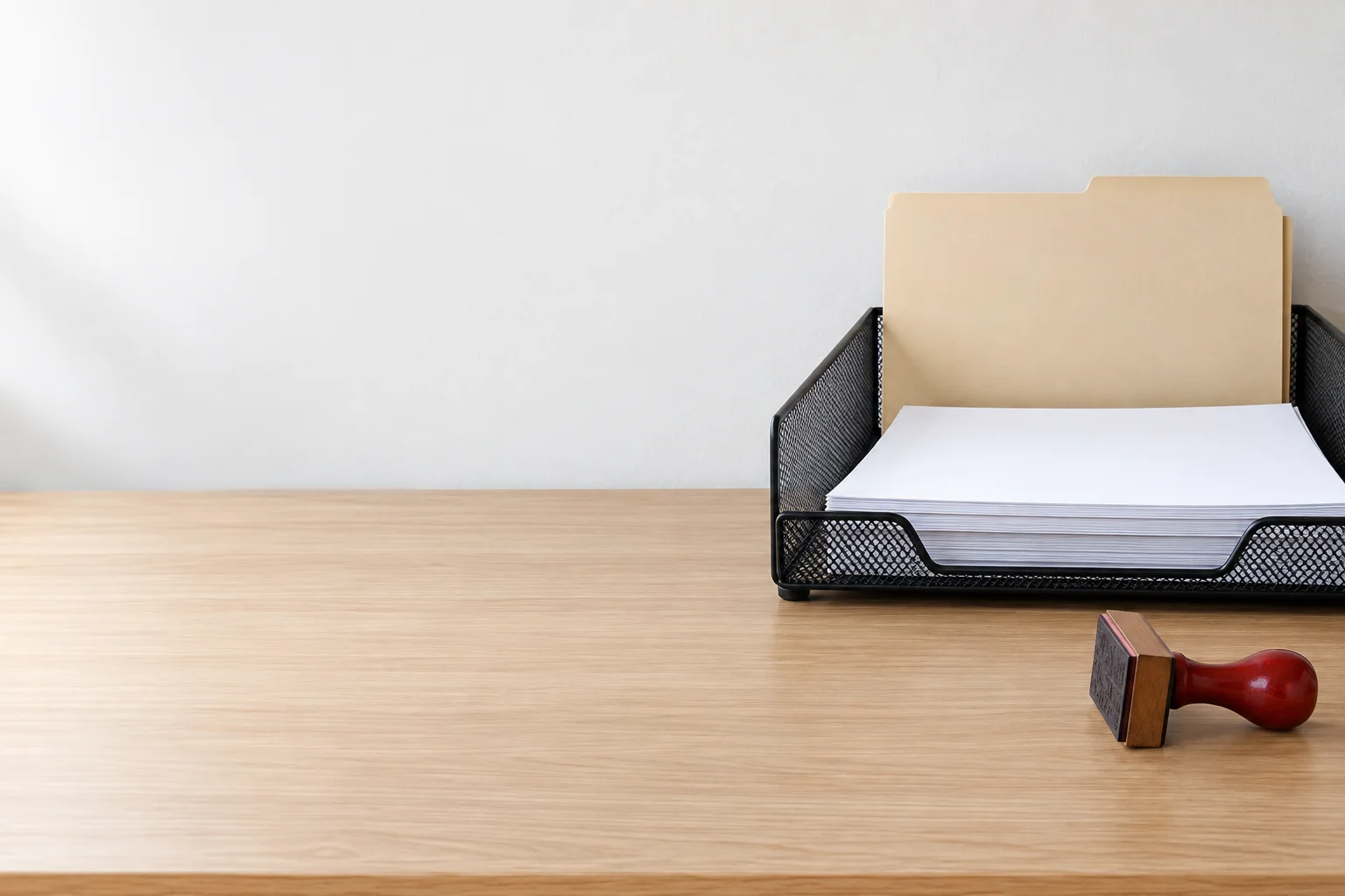 A wire in-tray with a folder and papers, and a red rubber stamp